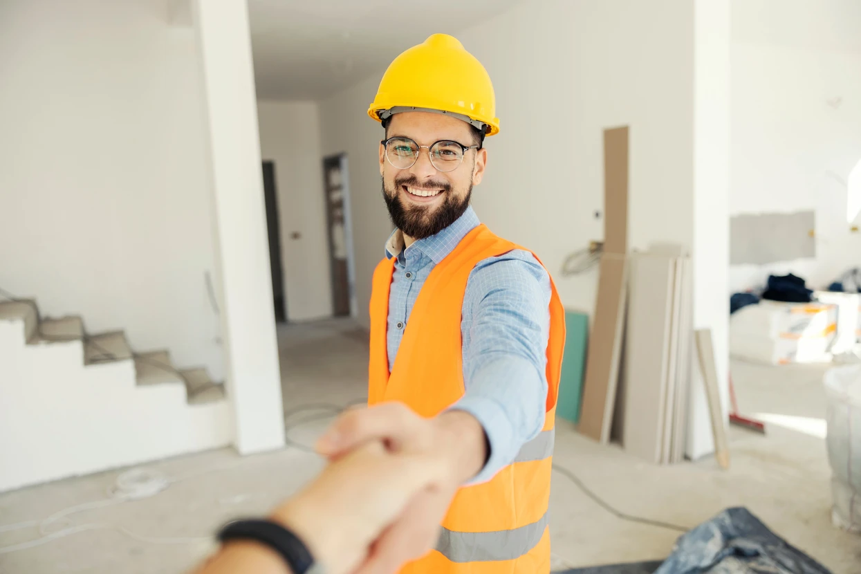 Portrait d'un ingénieur heureux en uniforme de protection serrant la main du client vers la caméra sur le chantier