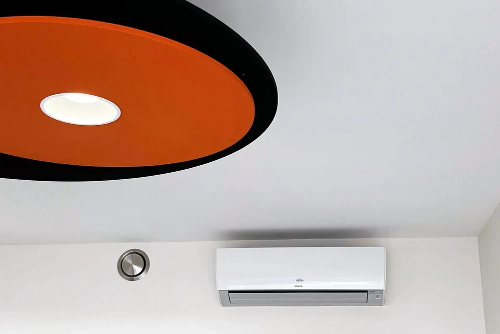 Intérieur moderne avec plafond blanc, climatiseur mural Fujitsu General installé, élément décoratif circulaire orange et noir au plafond avec éclairage LED intégré