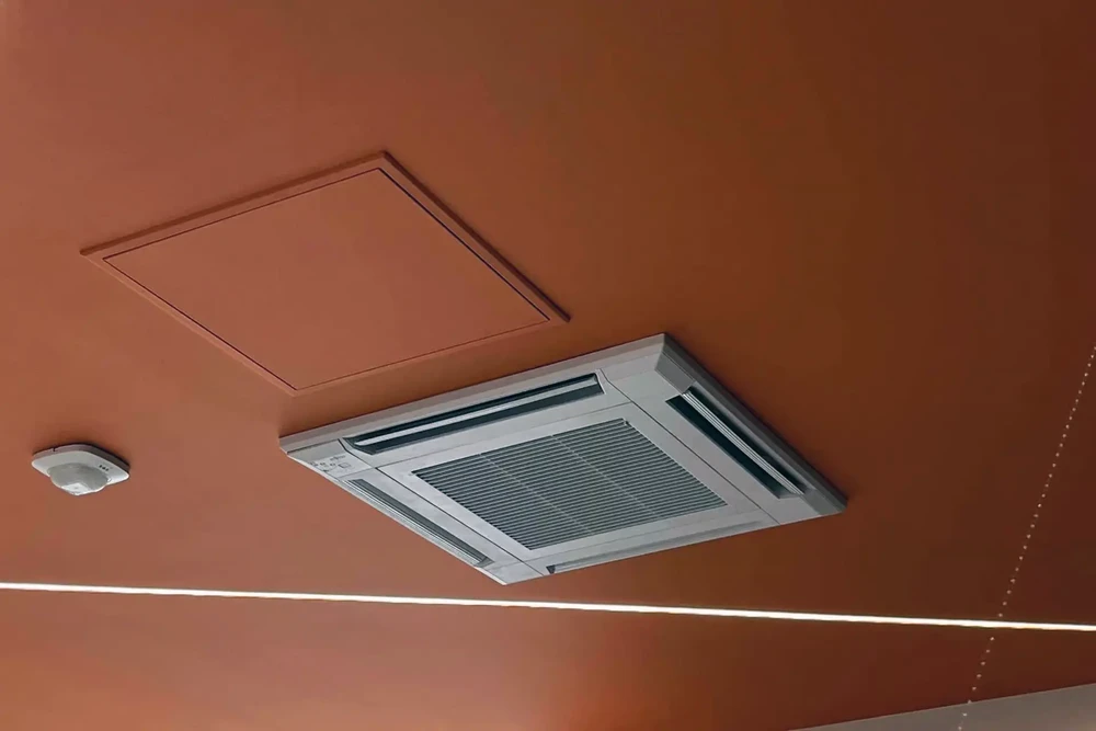 Intérieur commercial avec plafond orange, climatiseur cassette encastré blanc en fonctionnement, grilles d'aération visibles