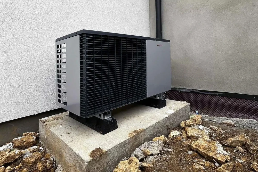 Extérieur résidentiel avec pompe à chaleur air-eau installée sur dalle béton surélevée près du mur de façade