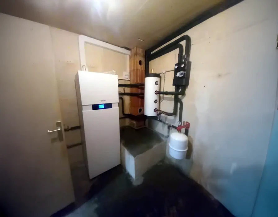 Local technique avec chaudière murale blanche moderne équipée d'écran digital, reliée à un ballon d'eau chaude sanitaire vertical par tuyauterie cuivre et raccords laiton