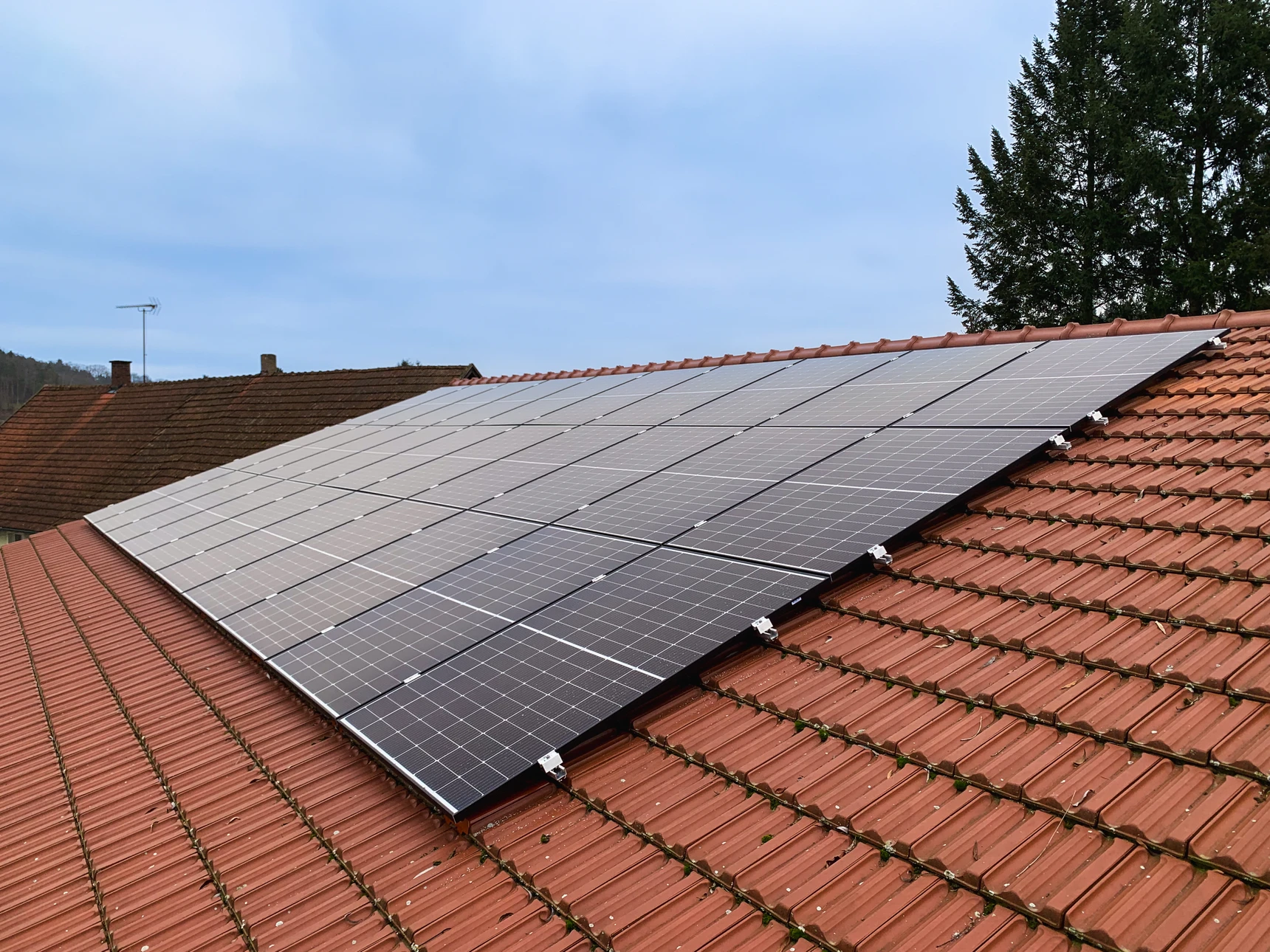 Extérieur résidentiel avec maison moderne équipée de panneaux solaires photovoltaïques noirs installés sur toiture en tuiles grises